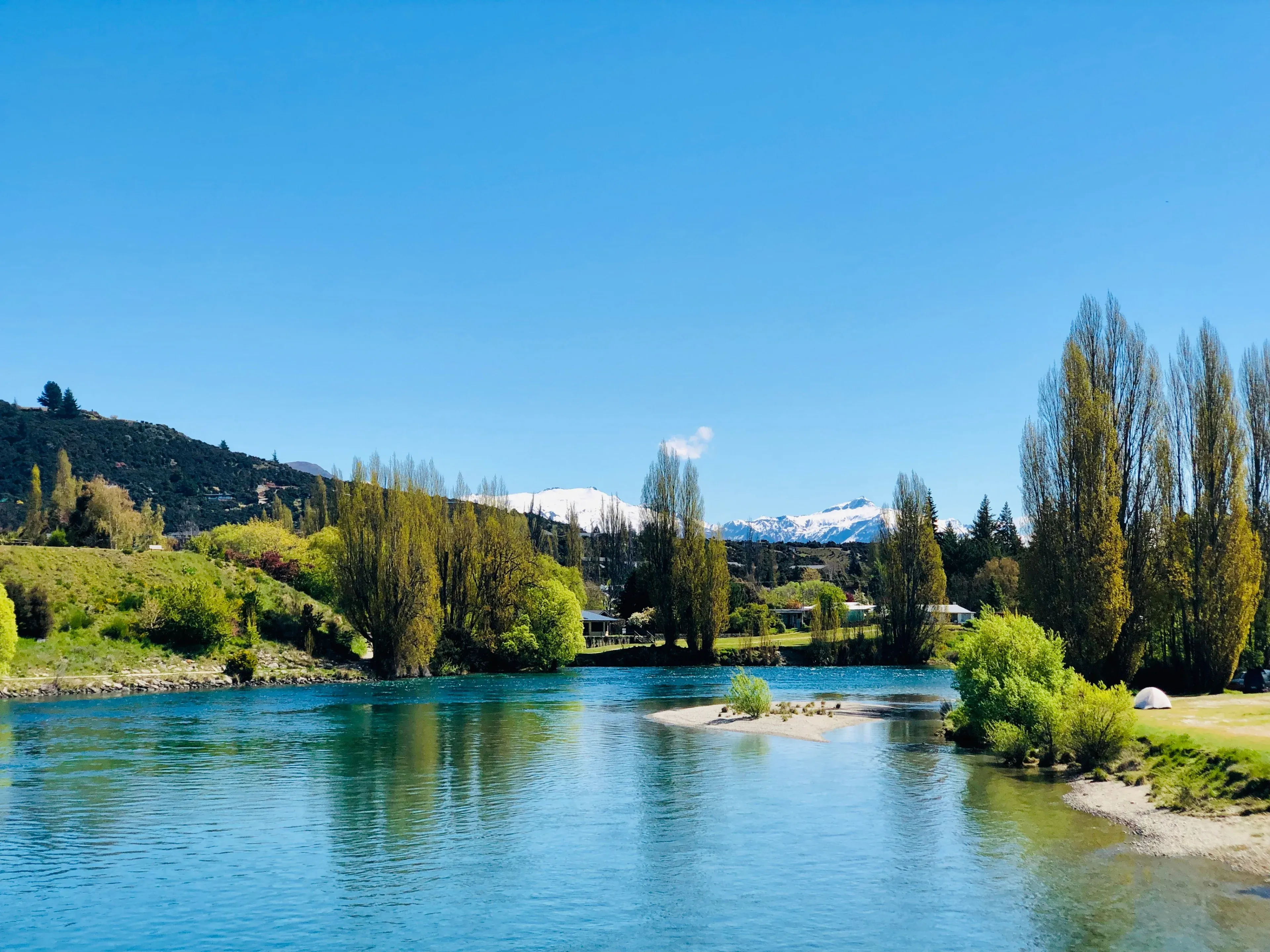 Picturesque Albert Town riverside with snowy mountain views and vibrant poplar trees in New Zealand.