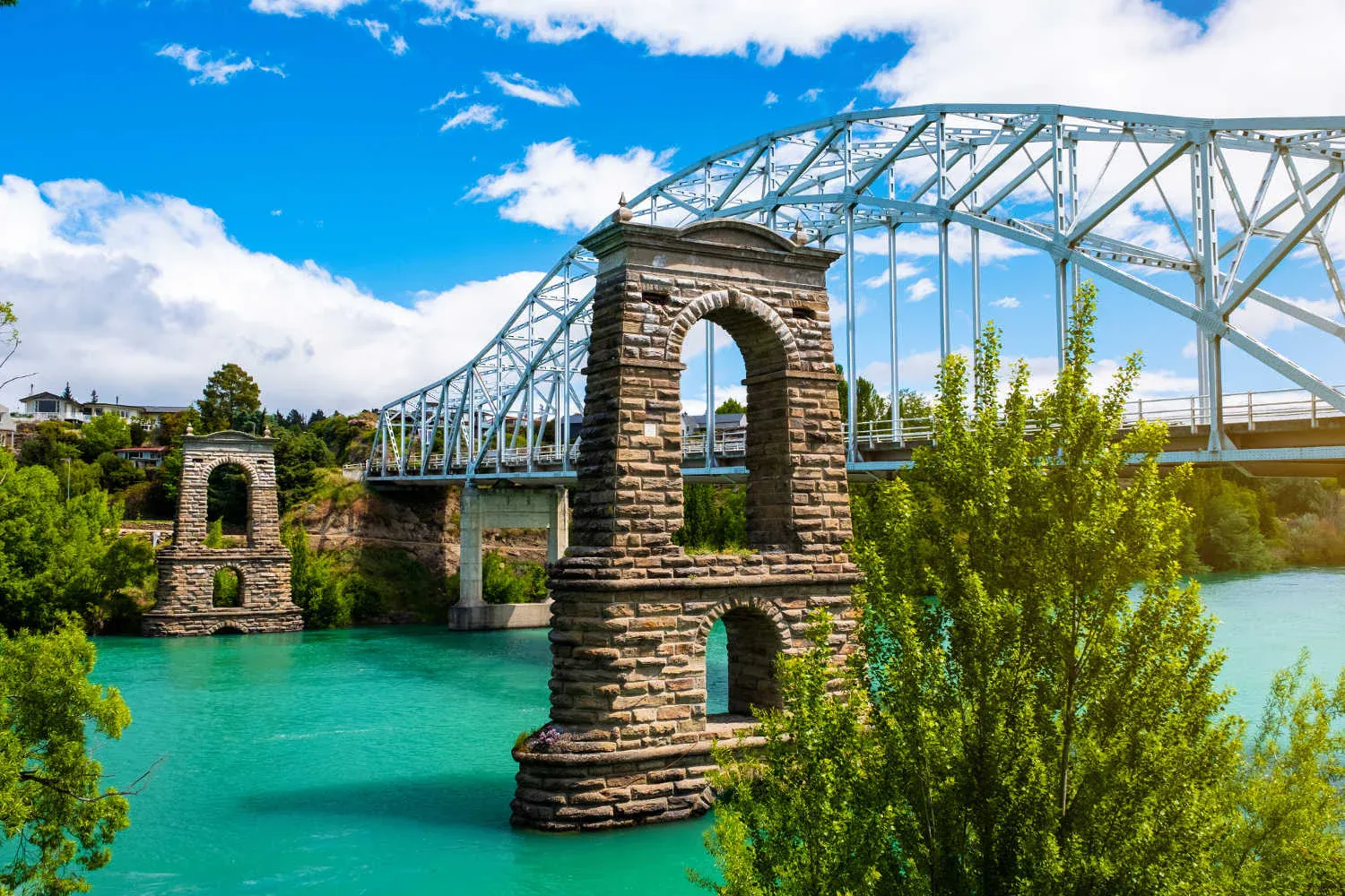 Stunning Alexandra bridge over turquoise Clutha River, framed by lush greenery and historical architecture.