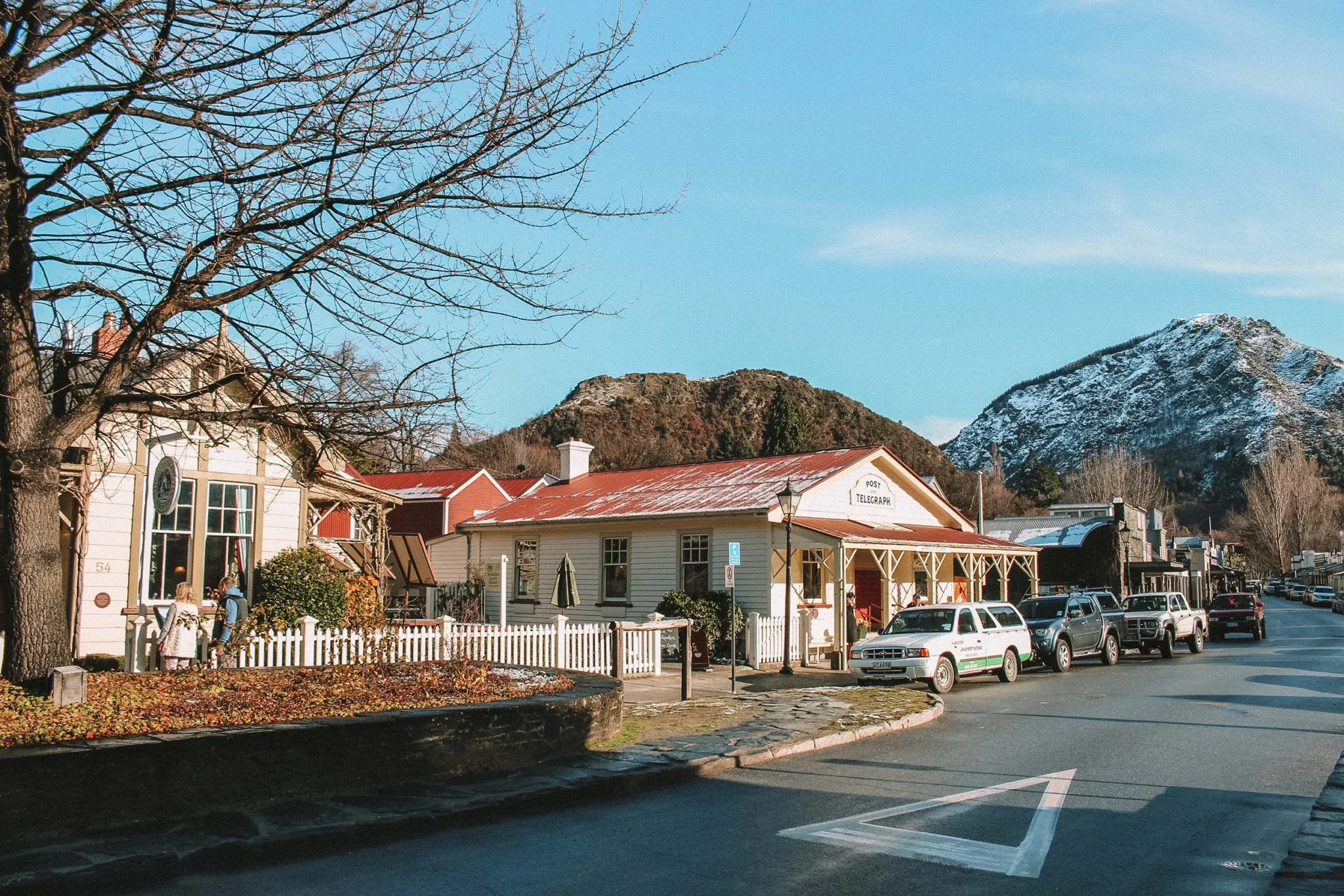 Historic Arrowtown streetscape with heritage buildings, vibrant trees, and mountain backdrop in New Zealand.