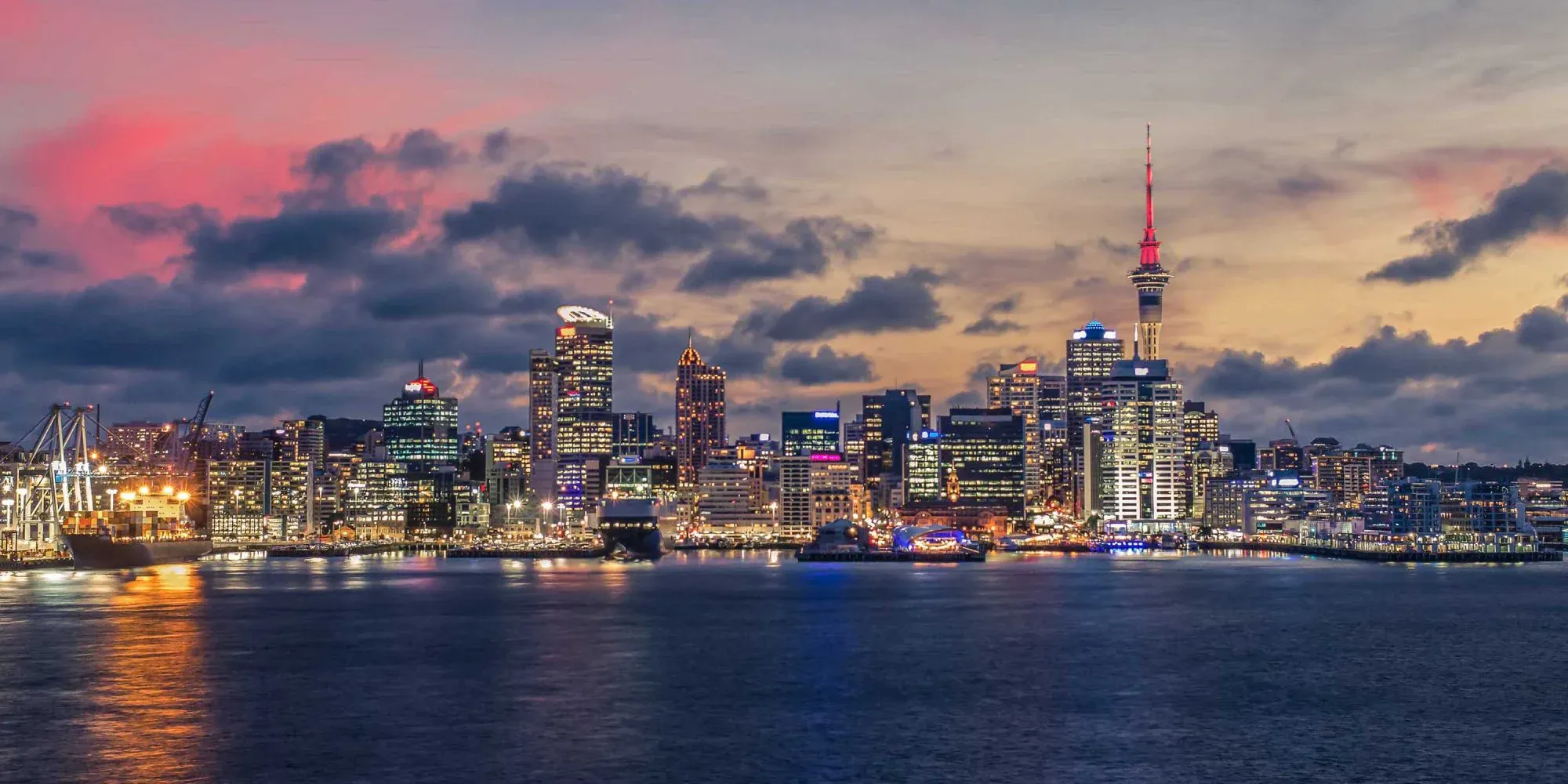 Auckland city skyline at twilight, featuring iconic Sky Tower and bustling waterfront in New Zealand.