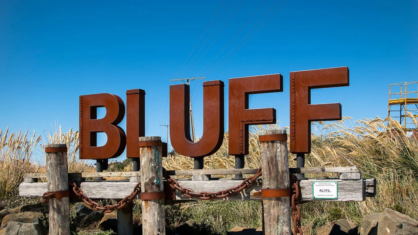 Bluff sign with rugged coastal backdrop, marking New Zealand's southernmost town and a seafood hub.