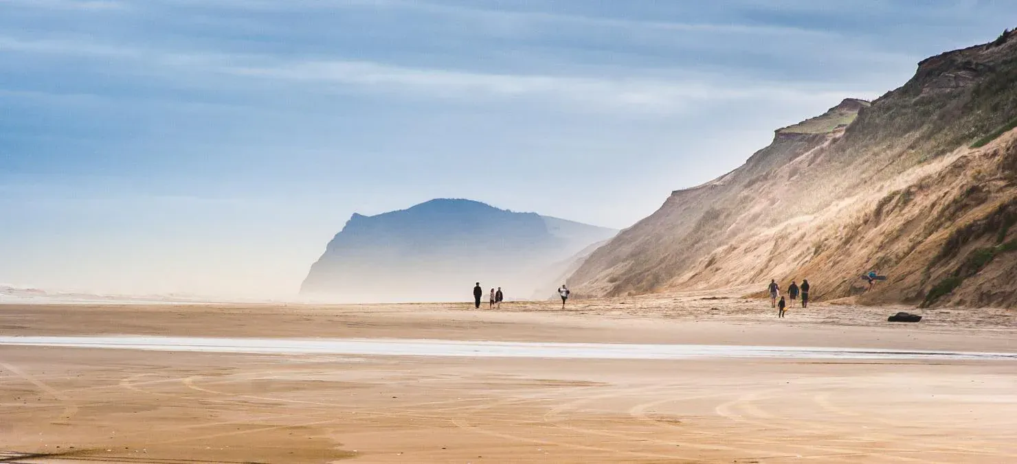 Dargaville's golden beach with walkers, promoting local hospitality and tourism businesses.