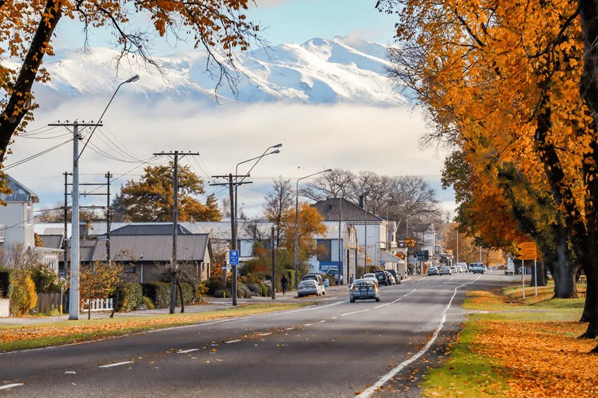 Fairlie main road with autumn trees and Southern Alps, highlighting hospitality and retail businesses.