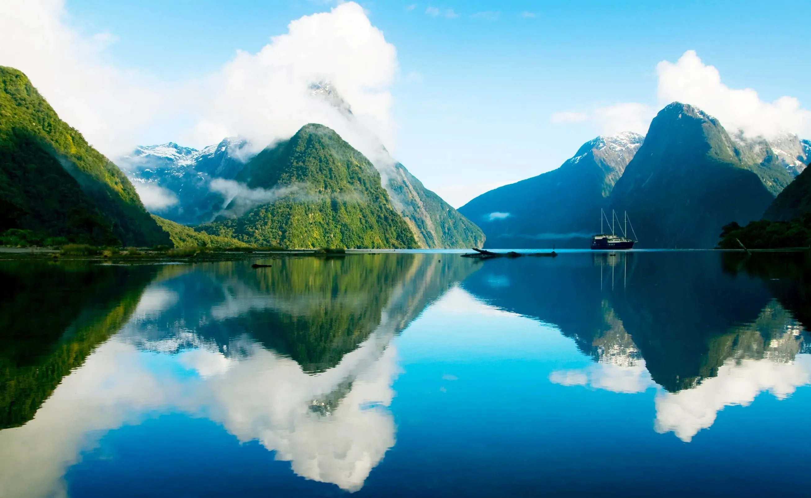 Mountains near Milford Sound, New Zealand, reflecting off a lake with clear blue skies