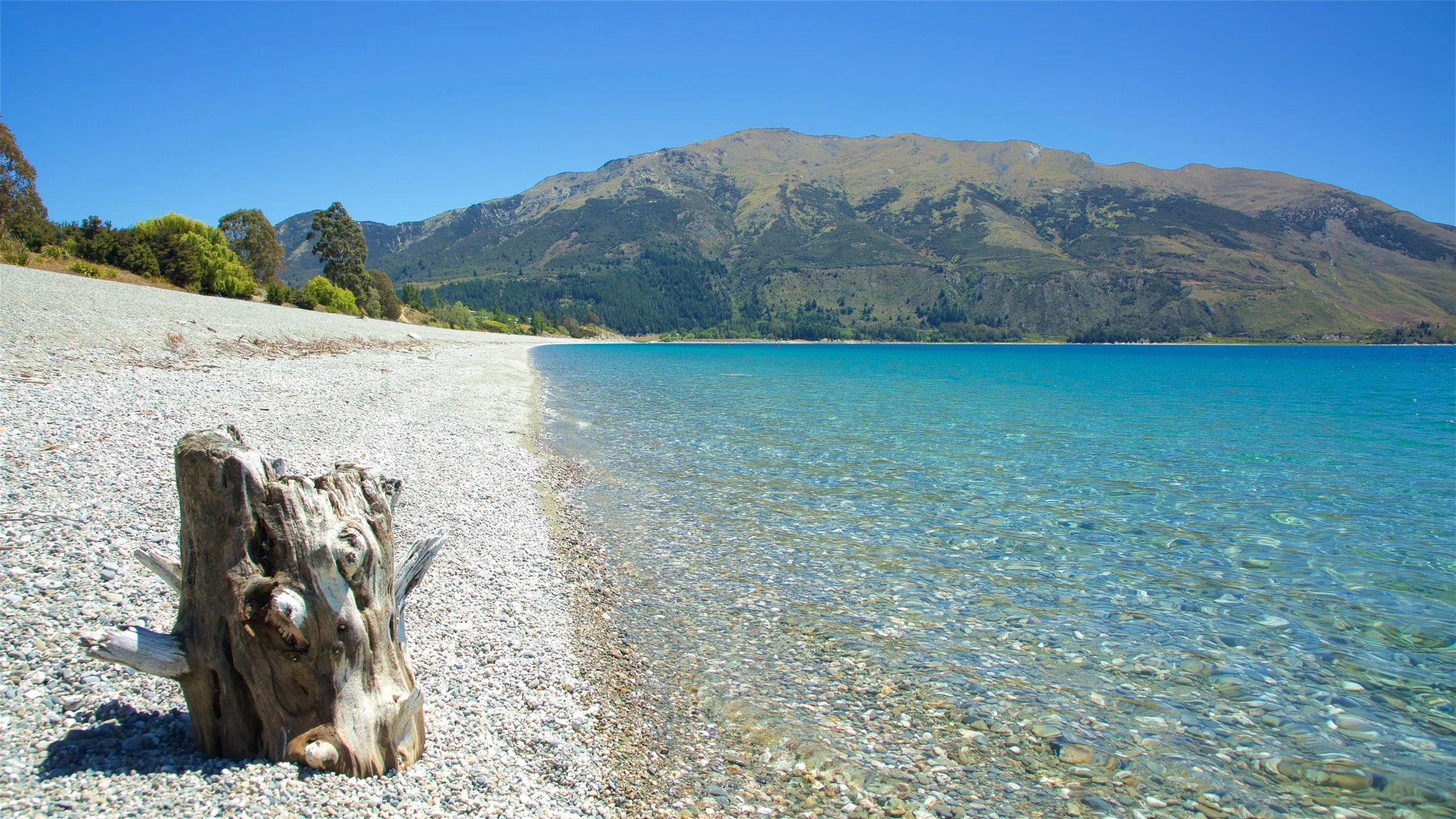 Lake Hawea's crystal-clear waters and pebble shoreline with scenic mountains in the distance.