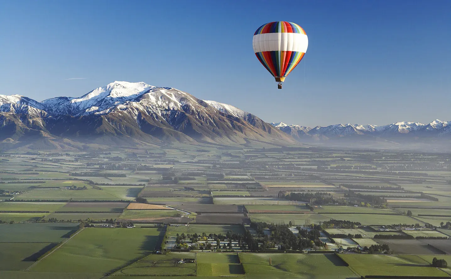 Hot air balloon over Methven with snow-capped Southern Alps in the background, a serene Canterbury town.